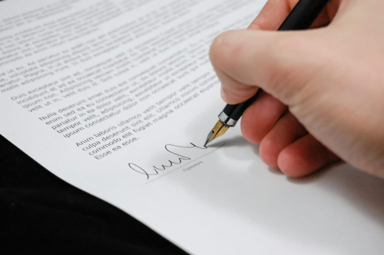Home Close-up of a hand signing a legal document with a fountain pen, symbolizing signature and agreement.