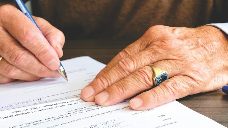 Home Close-up of a senior adult signing a legal document with a focus on hand and gold ring.