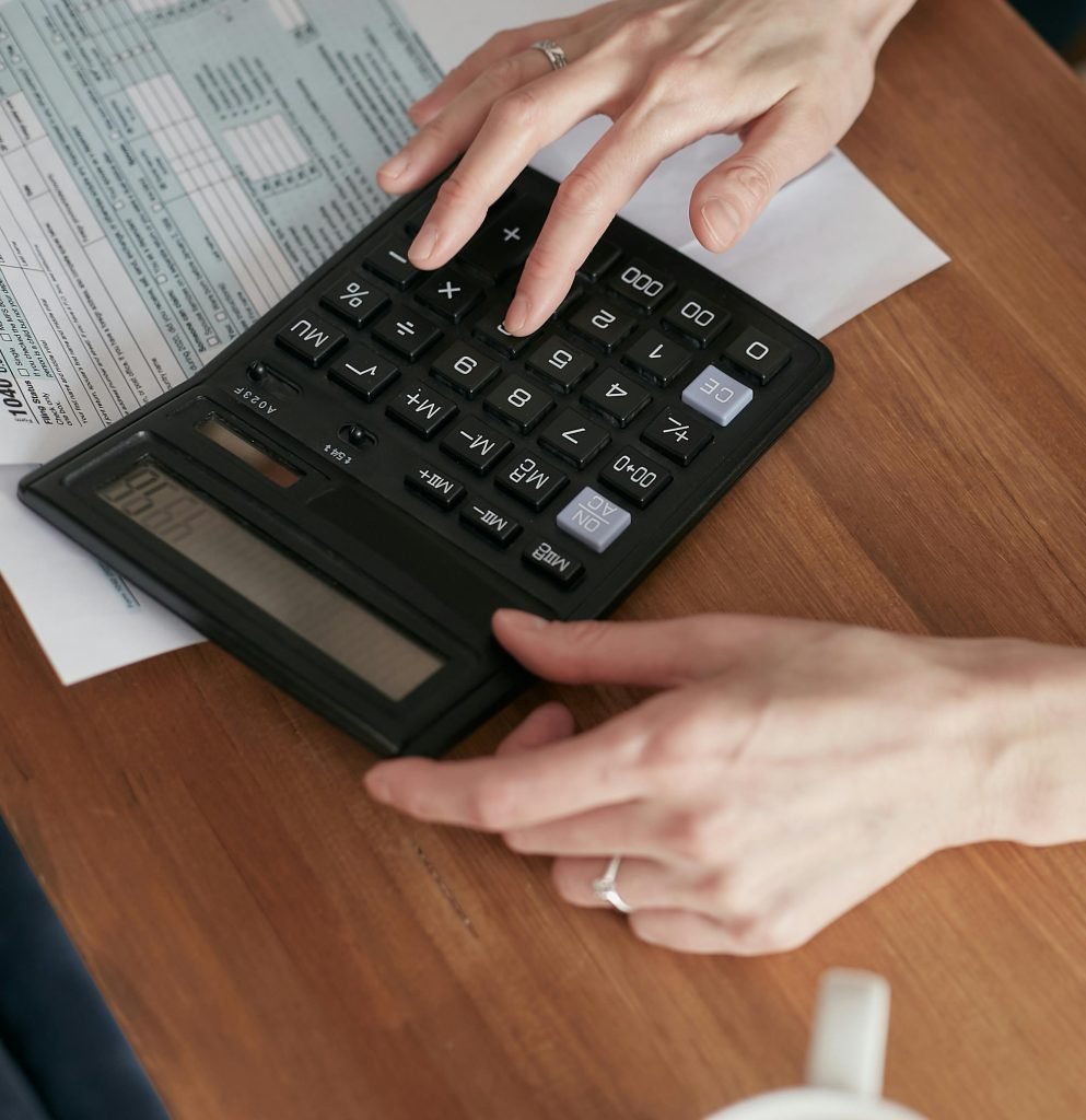 Person calculating finances with a calculator and document on a wooden desk.